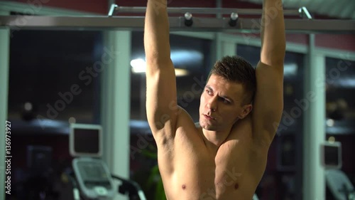 Young attractive adult man in a fitness gym. He rests between exercises and looking at side. Sport training indoors photo