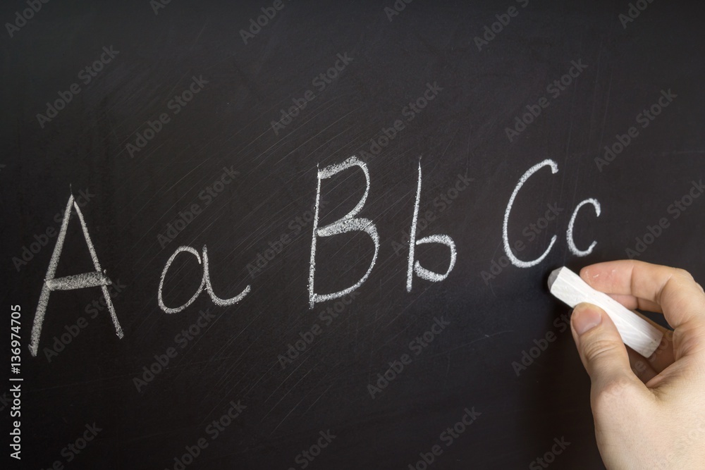 Teacher is writing letter of alphabet on blackboard with chalk. Education in elementary school concept. Teacher is writing letter of alphabet on blackboard with chalk. Education in elementary school concept.