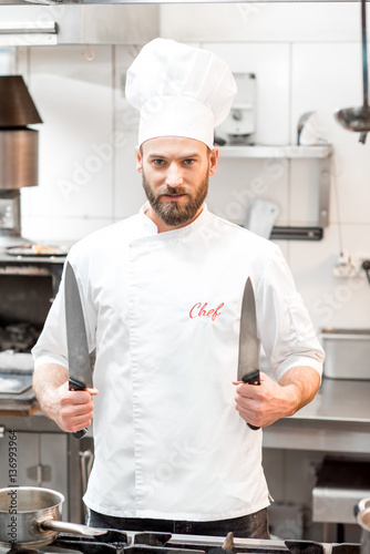 Portrait of chef cook in uniform with knifes at the restaurant kitchen