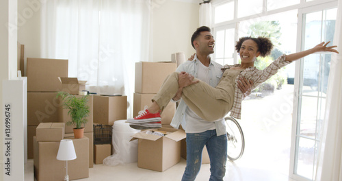 Ecstatic young couple celebrating their new home with the young man holding his wife in his arms as she grins and laughs at the camera