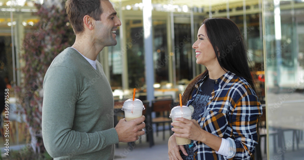 Young couple drinking takeaway beverages standing side by side enjoying a quiet chat outdoors in an urban street Young couple drinking takeaway beverages standing side by side enjoying a quiet chat outdoors in an urban street