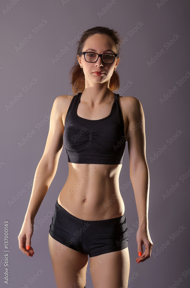A slender woman in a sports top and shorts on a gray background. A slender woman in a sports top and shorts on a gray background.