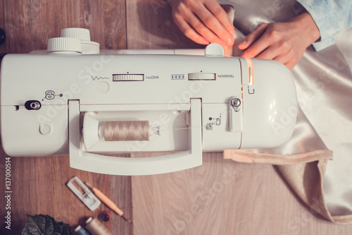 top view of the hand of a girl who is sewing at the sewing machine, see the desktop and the fabric