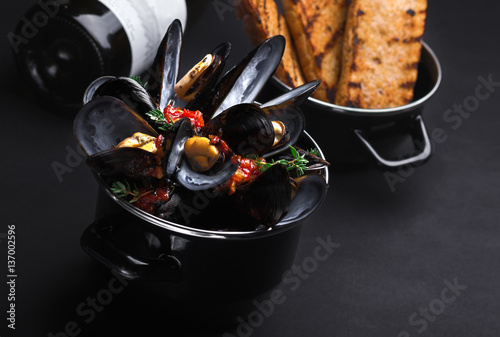 Casserole with mussels. a bottle of wine and a baguette, black background. photo