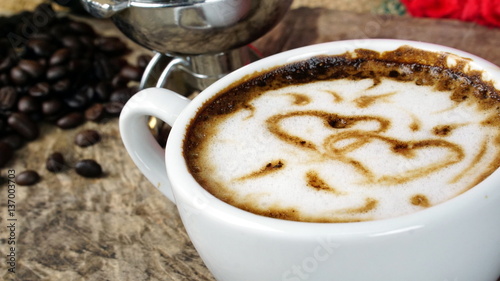 Cappuccino coffee and sweet love with hearts. A cup of latte, cappuccino or espresso coffee with milk put on a wood table with dark roasting coffee beans. Drawing the foam milk on top.