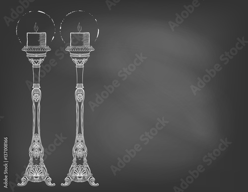 Two highly ornamental candles on chalkboard