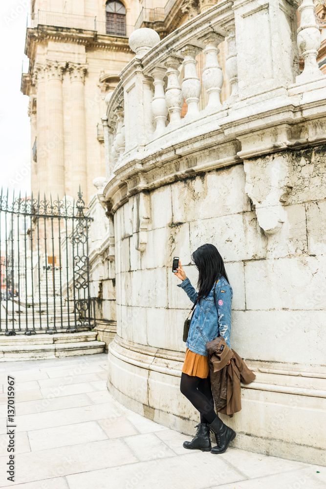 Young woman taking a selfie photo in front of the the Renaissance Cathedral in Malaga, Andalusia, Spain