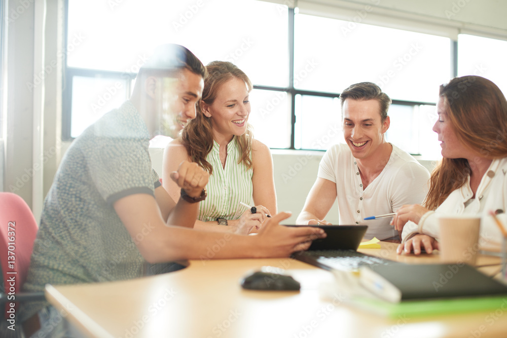 Unposed group of creative business entrepreneurs in an open concept office brainstorming together on a digital tablet. Unposed group of creative business entrepreneurs in an open concept office brainstorming together on a digital tablet.