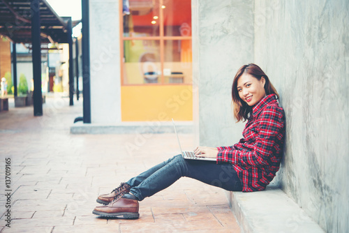 Happy young hipster woman using her laptop while sitting on the steps.