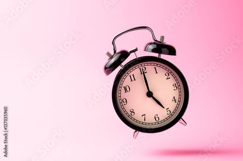 black vintage alarm clock floating on the air with pink color ba