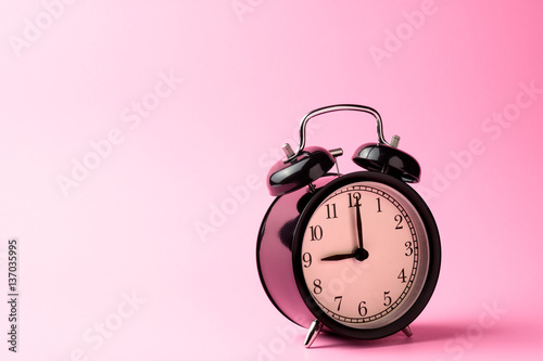black vintage alarm clock on pink color background