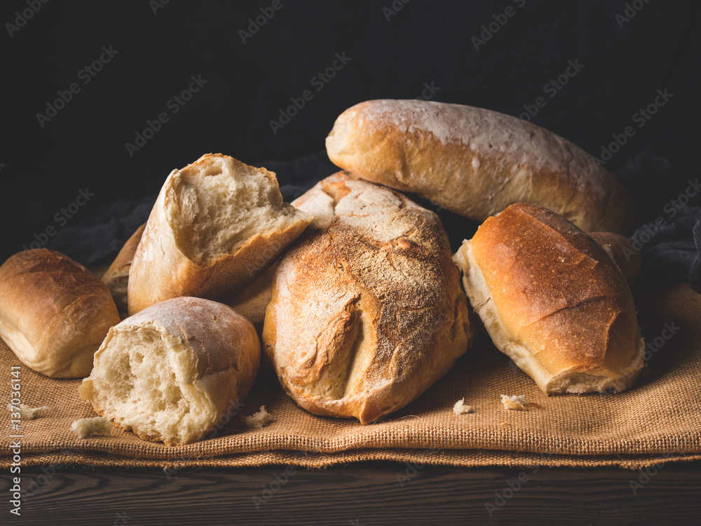 Freshly baked bread loaves on burlap dark wooden background. Texture closeup italian bakery products