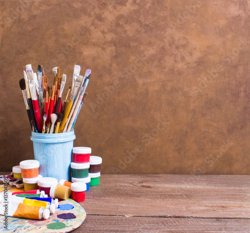 Paints, brushes and palette on the brown wooden background. The workplace of the artist. Banner for school