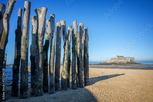 Wood piles at low tide, Fort National in the background, on the beach of Saint Malo, France