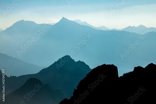 Spectacular blue and cyan mountain ranges silhouettes. Summit crosses visible.