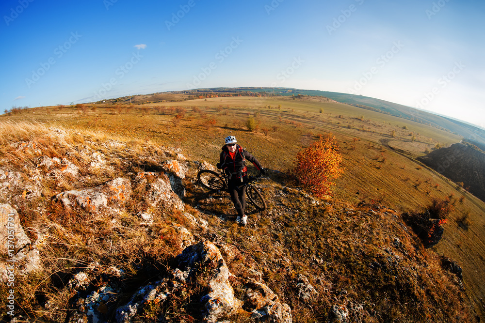 Fisheye of cyclist standing with mountain bike at sunrise against bright sun and blue sky.