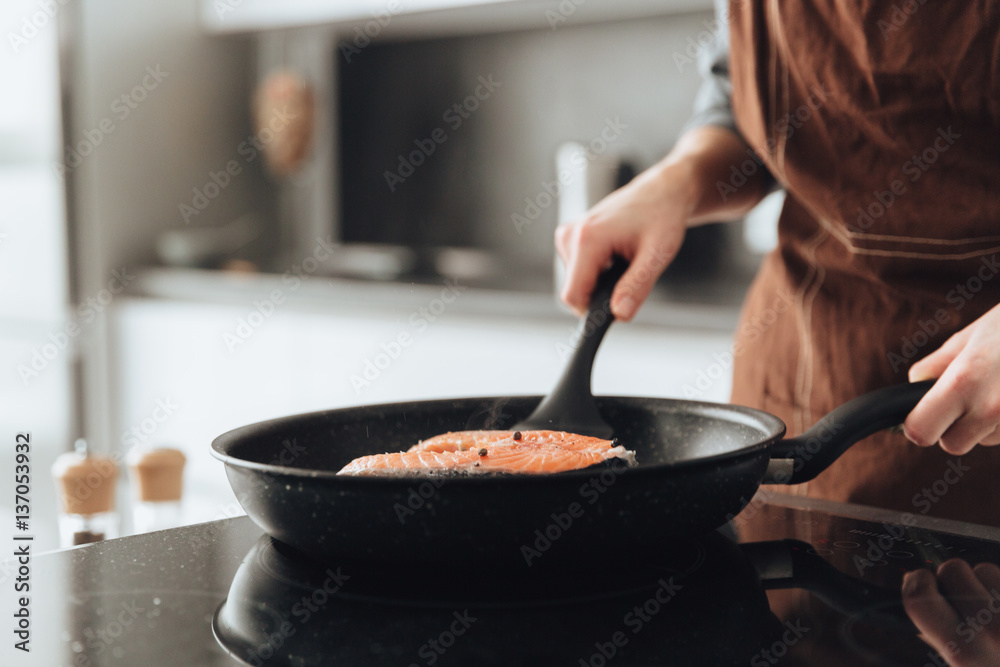 Cropped image of young lady cooking fish. Cropped image of young lady cooking fish.