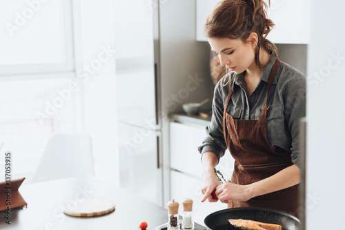 Pretty lady standing in kitchen while cooking fish