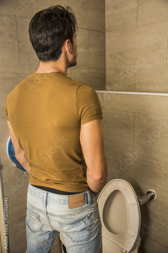Canvas Print Rear View of a Young Man in Black Outfit Peeing at the Toilet Inside his Bathroom