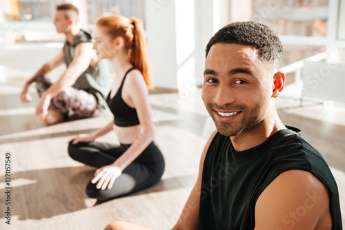 Cheerful african american young man practicing yoga in group