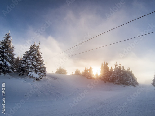 Hazy dieing sun on a ski slope with icy snow covered trees