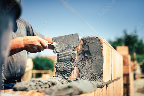 Fototapeta Bricklayer construction worker installing brick masonry on exterior wall with tr