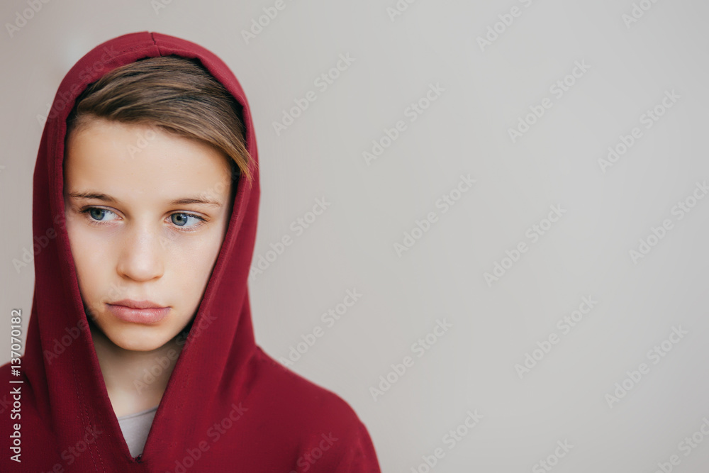 Young attractive boy in red hoodie looks away on a light background Young attractive boy in red hoodie looks away on a light background