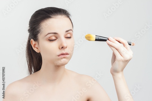 Nude brunette with closed eyes holding makeup brush