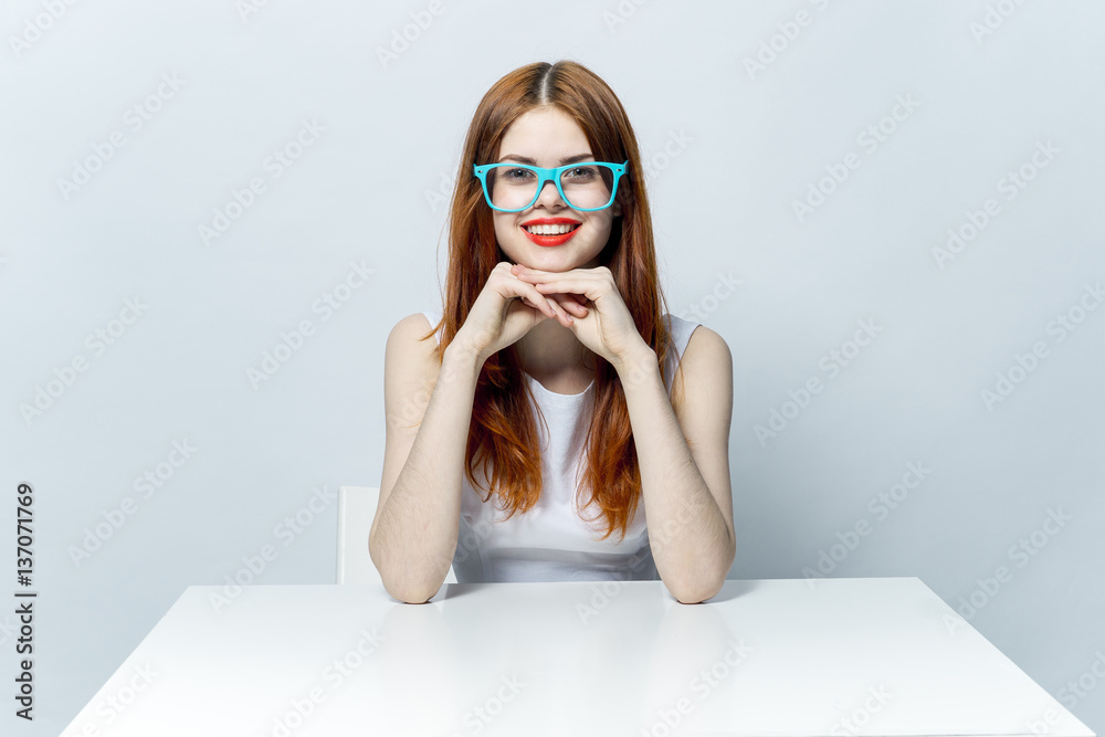 smiling woman sitting at a table in big blue glasses smiling woman sitting at a table in big blue glasses