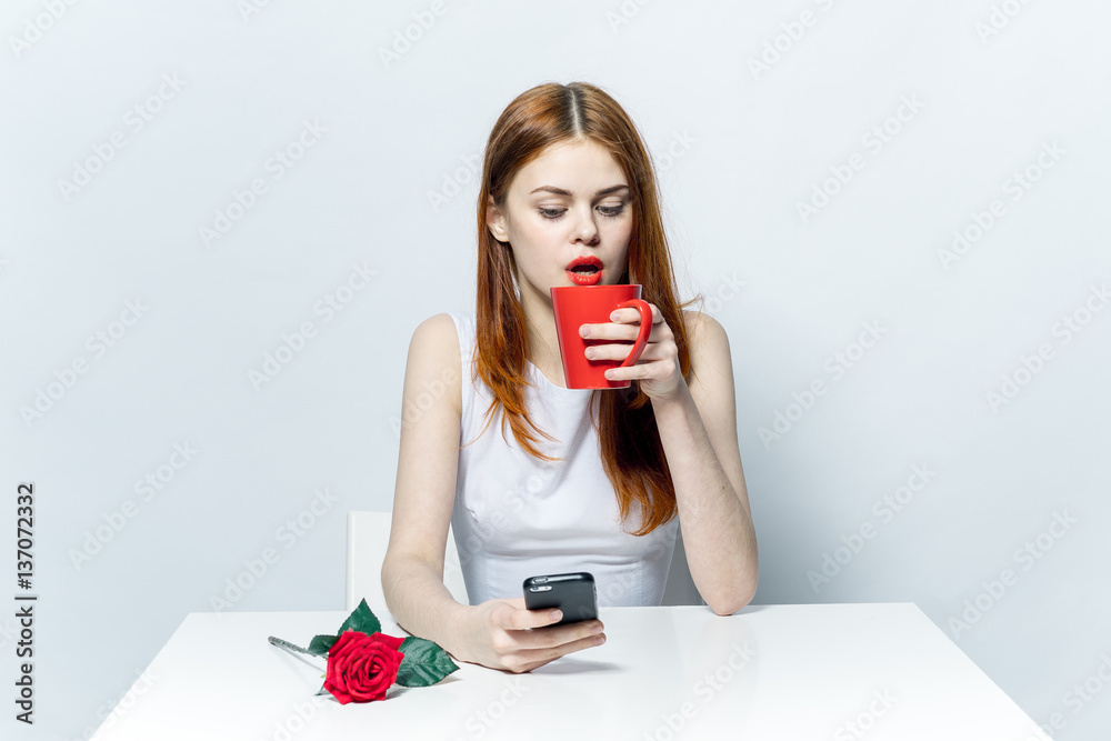 woman sitting at table drinking from mug and looking into phone woman sitting at table drinking from mug and looking into phone