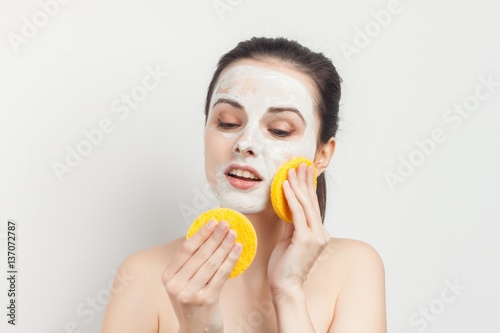 woman wipes cream from face with yellow sponges