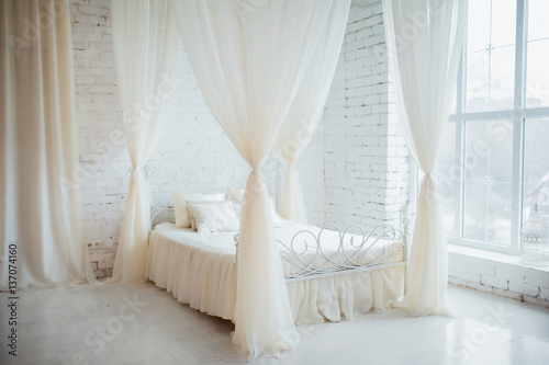 Bedroom in soft light colors. Big comfortable elegant double bed in white brick loft interior with large window