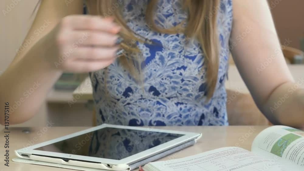 Student sitting at desk views photos using silver computer tablet indoors. Close-up Student sitting at desk views photos using silver computer tablet indoors. Close-up
