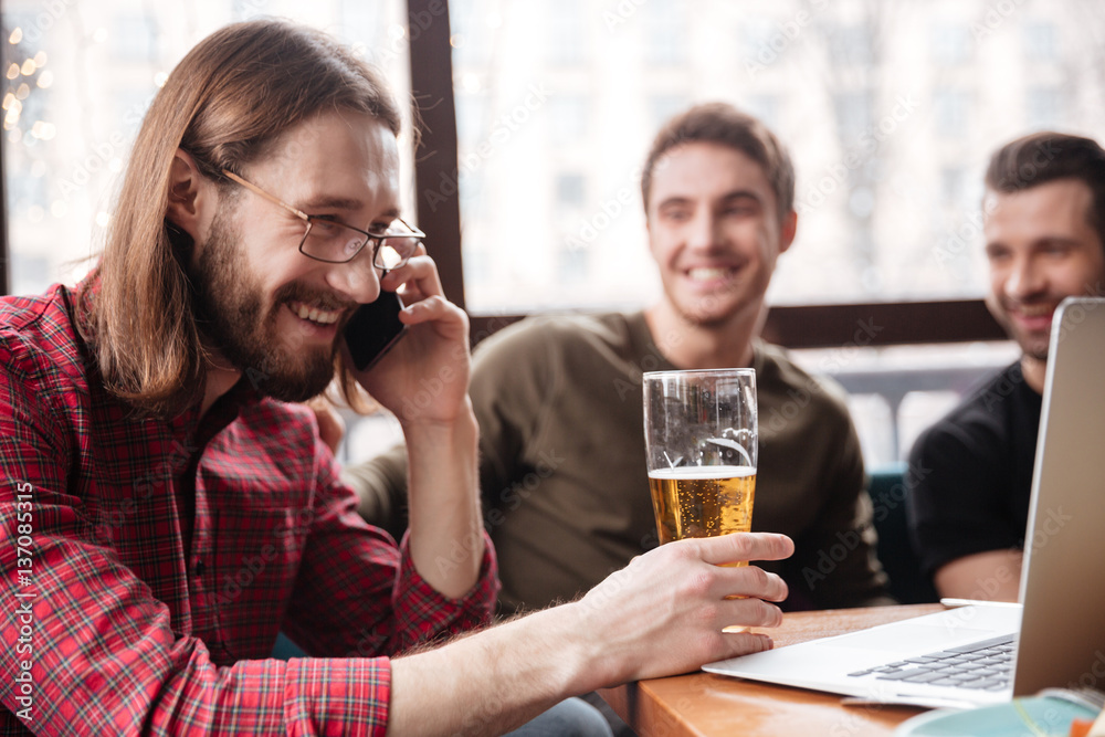 Men friends sitting in cafe drinking beer. Talking by phone.