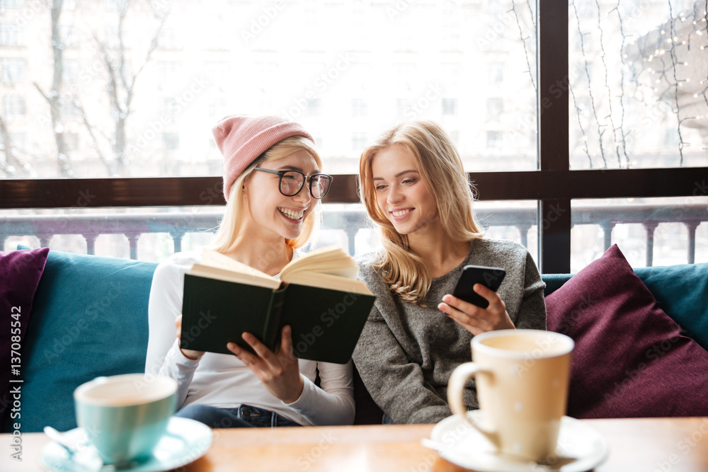 Happy two women friends sitting in cafe and reading book Happy two women friends sitting in cafe and reading book