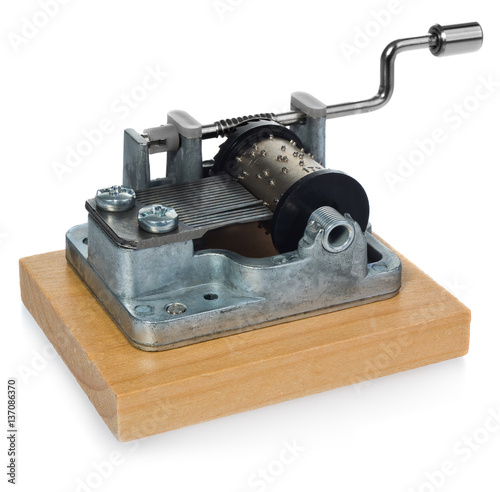 The mechanism of silver music box with a handle on a wooden board. Musical toy in a side view, at an angle on a white background with light reflection.