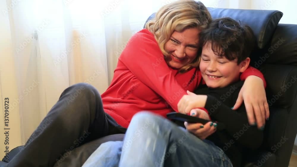 Mother and her young boy having fun while watching tv at home Mother and her young boy having fun while watching tv at home