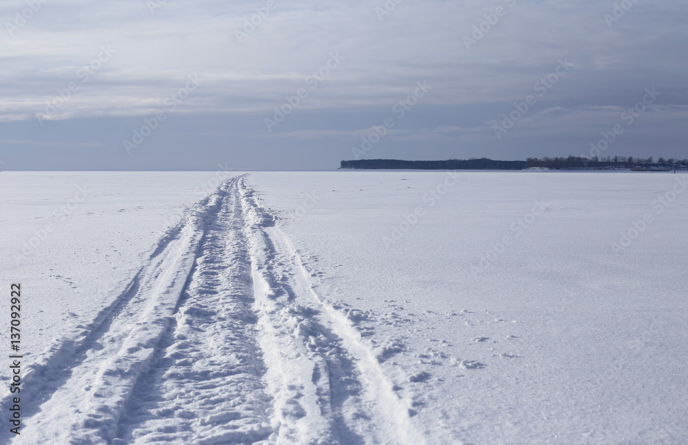 ice and soft snow on a large river. narrow path leaves far forward. against the background of the shore and clouds.