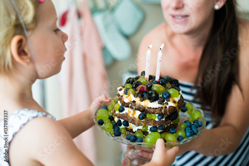 Mother giving her cute daughter birthday cake with candles