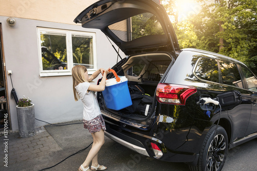 Girl loading cooler in black car trunk against house photo