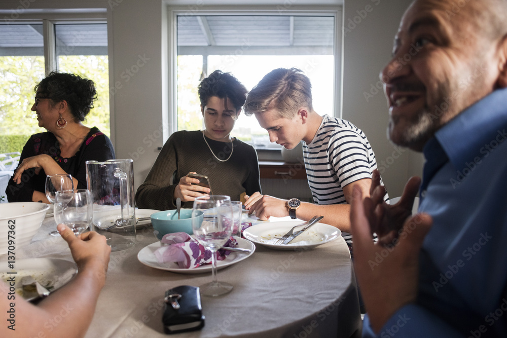 Friends using phone while family talking at dining table in dinner party Friends using phone while family talking at dining table in dinner party