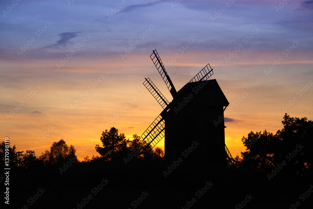 Silhouettes of wooden windmills and trees on sunset backgrounds