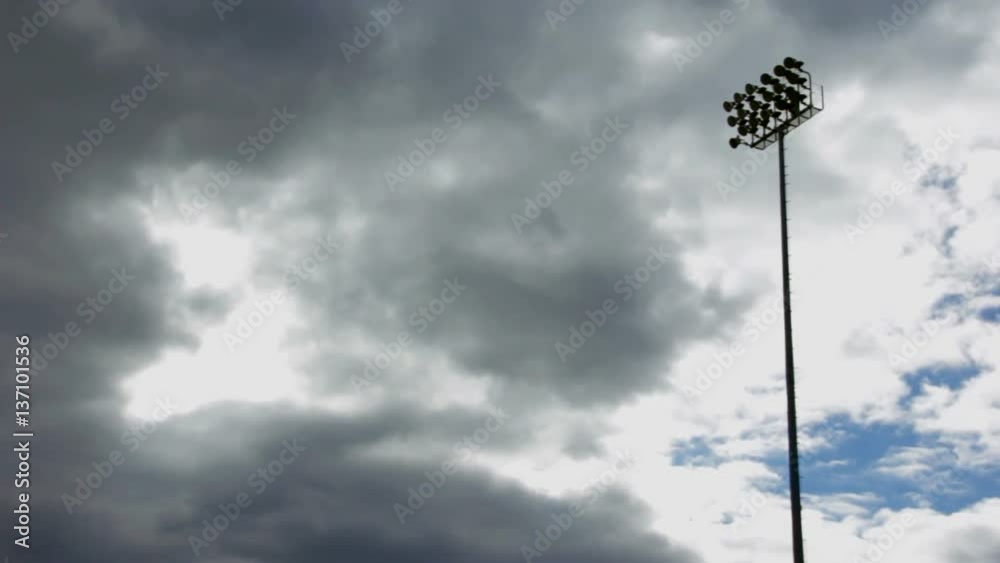 Pan of shilouetted stadium lights during the day, with gloomy clouds passing by.