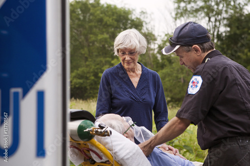 Paramedic and senior woman standing next to senior patient lying on stretcher