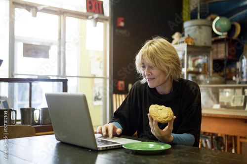 Woman sitting at table using laptop and holding sugarcookie photo