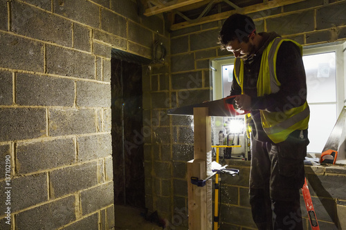 A builder on a home build site using a saw on a block of wood. 