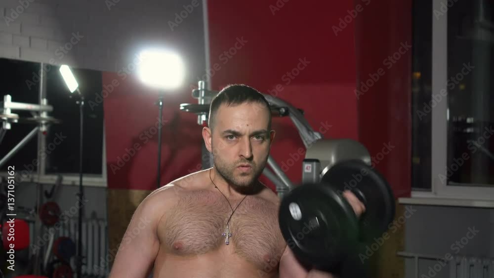 The man lifts heavy dumbbells in the gym. The man trains in weights. The man swings hands. Strong sports man. Close up The man lifts heavy dumbbells in the gym. The man trains in weights. The man swings hands. Strong sports man. Close up