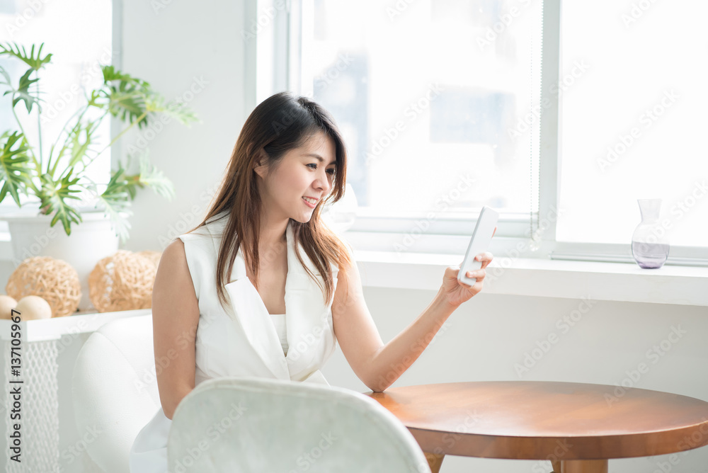 Happy Asian woman smiling while using smart phone in white room Happy Asian woman smiling while using smart phone in white room