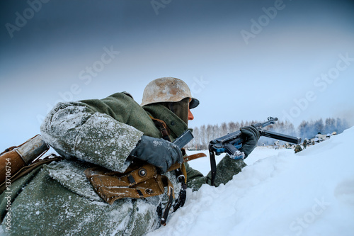 German Wehrmacht Soldier is reloading his submachine gun. Reconstruction of the winter defensive battles of the Red Army in WWII (1944 year). photo