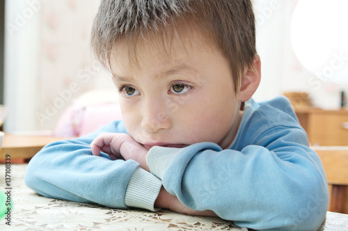 Sad boy portrait looking away thinking sitting on the table, thoughtful child feeling hurt